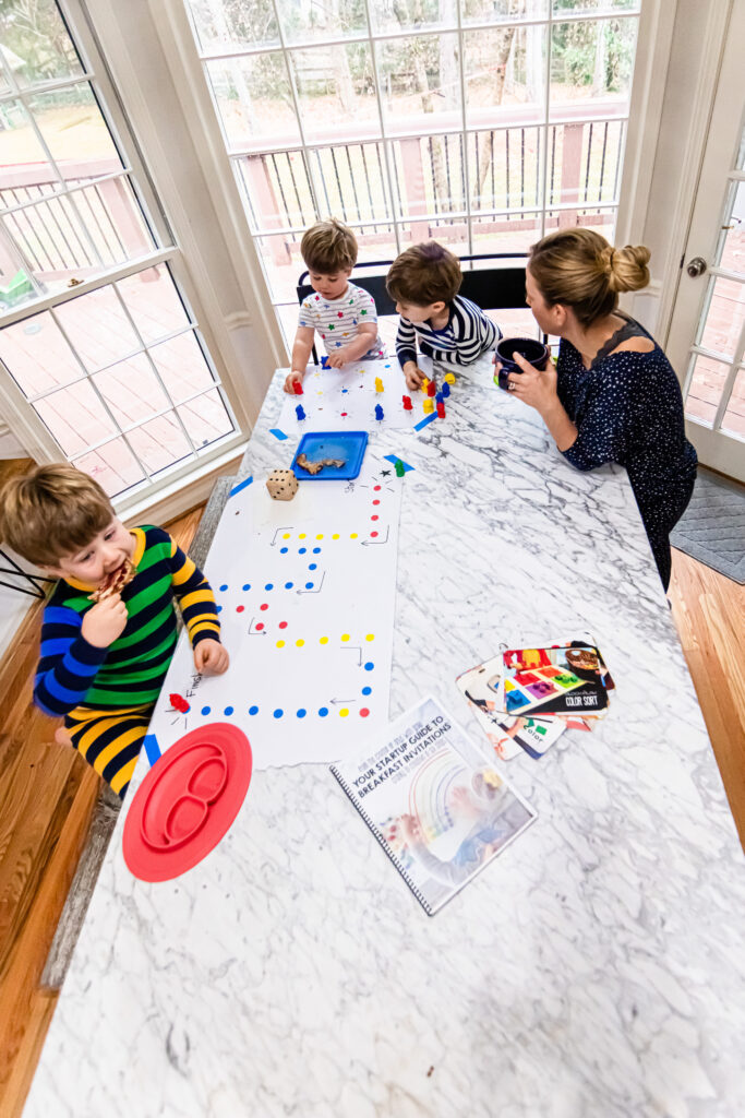 Mom with three kids at the breakfast table. They are working on a simple game as she is sipping coffee.